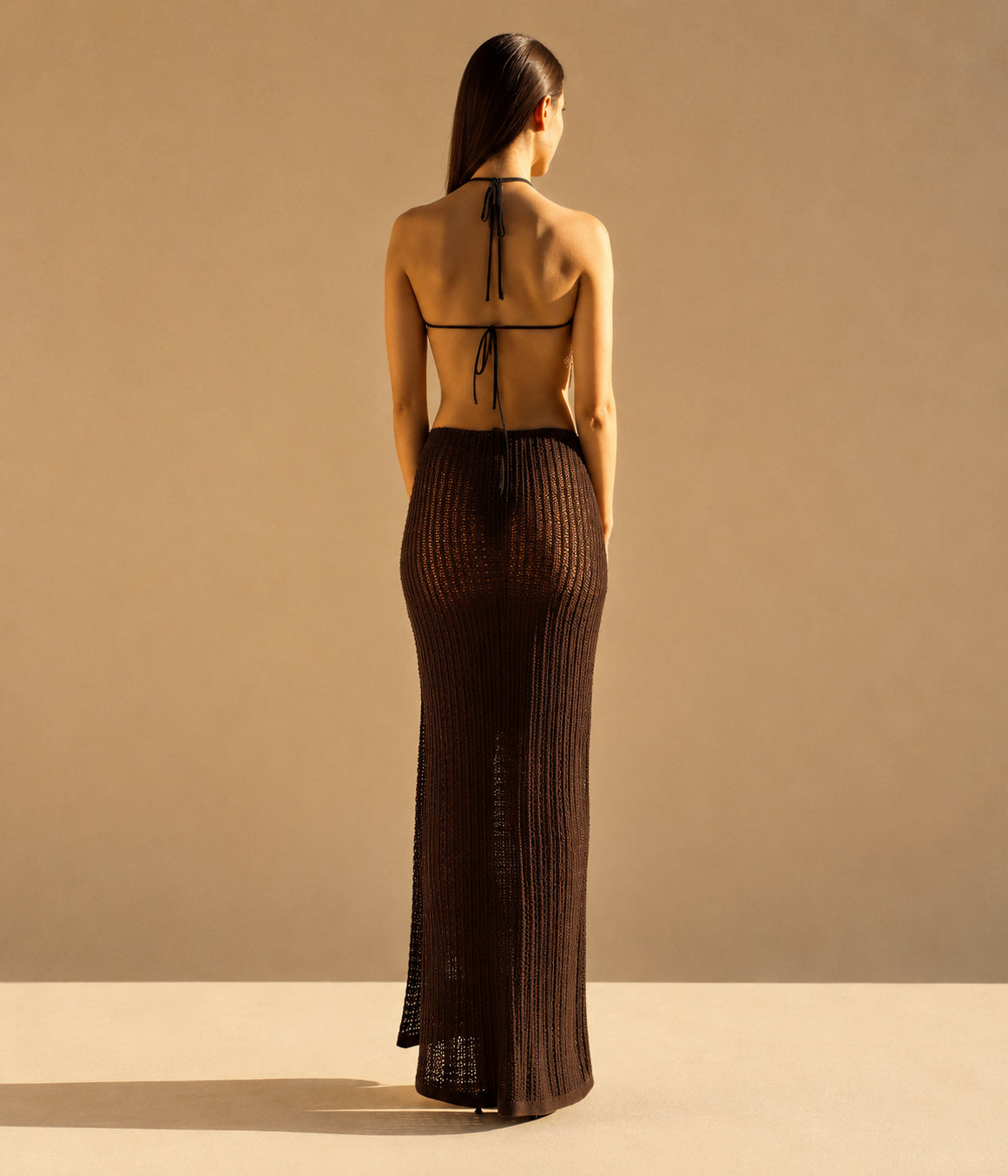 Woman wearing a brown ribbed dress with a backless design on a beige background